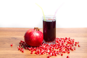A glass of delicious pomegranate juice, pomegranate and pomegranate seeds on a table