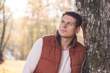 Mann lehnt nachdenklich an einem alten Baum im Park