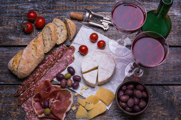 Fototapeta na wymiar Red wine in a glass and a set of products - cheese, sausage, salami, olives, tomatoes, hot peppers, bread on a wooden board, background
