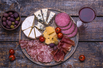 Red wine in a glass and a set of products - cheese, sausage, salami, olives, tomatoes, hot peppers, bread on a wooden board, background