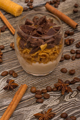 Yogurt desserts with chocolate and cookies, cinnamon sticks, cocoa beans, star anise on wooden background