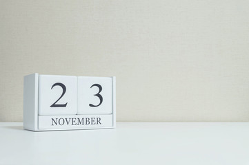 Closeup white wooden calendar with black 23 november word on blurred white wood desk and cream color wallpaper in room textured background with copy space , selective focus at the calendar