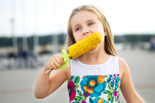 Adorable funny girl eating corn on the cob on sunny summer day