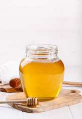 Glass jar of honey and wooden dipper on white