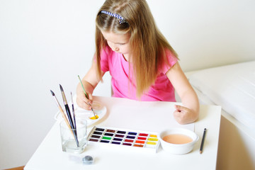 Adorable girl painting with watercolor in a sunny white room at