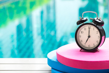 swimming times, retro black bell clock time at 7 o'clock at swimming pool blur background.