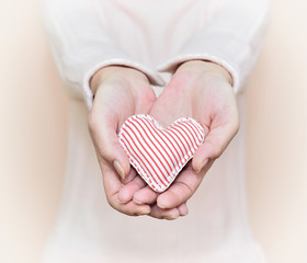 Hands of a woman showing a gift: little heart with red and white stripes. Selective focus.