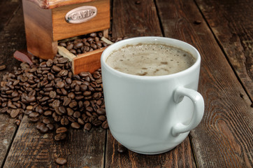 Coffee cup with grinder and beans on dark table