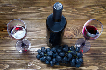 bottle of red wine,  wine glasses and grapes on wooden table