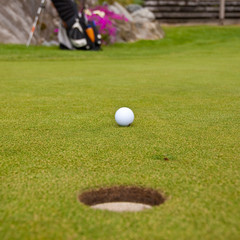 Golf ball on green with a hole. Shallow depth of field. Focus on the ball.