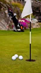 Three golf balls on green with flag. Shallow depth of field. Focus on the closest balla and the hole.