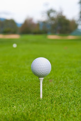 Golf ball on tee over a blurred green. Shallow depth of field. Focus on the ball.