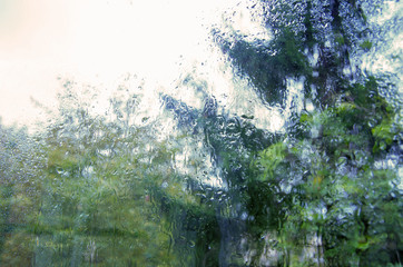 Raindrops on the glass with blurry natural green tree background