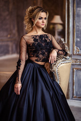 Beautiful young woman in gorgeous black evening dress with perfect makeup and hair style