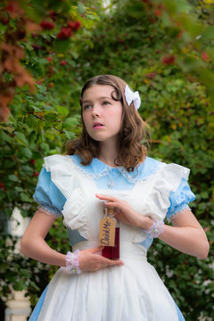 girl in image of fairy tale heroine drinks drink of glass bottle