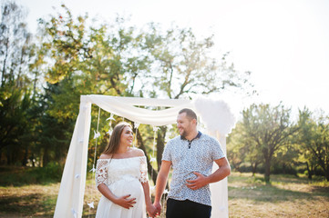 Happy pregnant couple stay hugging and loving near decor arch at