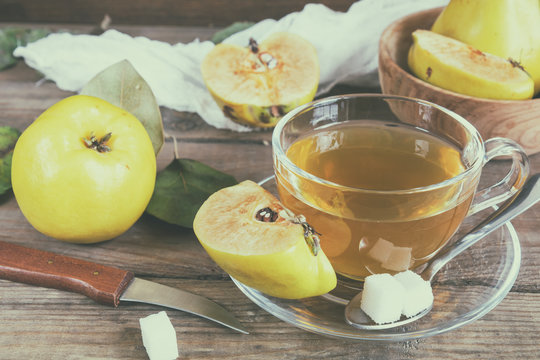 The cup of hot  tea and fresh quince fruit on dark wooden table. An autumn still life. Coloring and processing photo