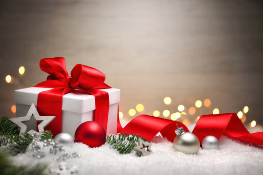 Weihnachten Hintergrund mit Geschenk und rotem Band, Lichtern, Kugeln, Tannenzweigen und Schnee