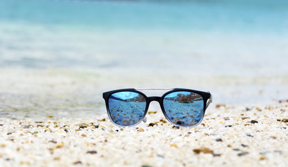 Fototapeta na wymiar Fashion blue sunglasses on sandy beach near the blue sea. Summer holiday concept