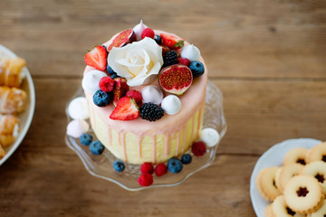 Cake with various berries, meringues and rose on cakestand.
