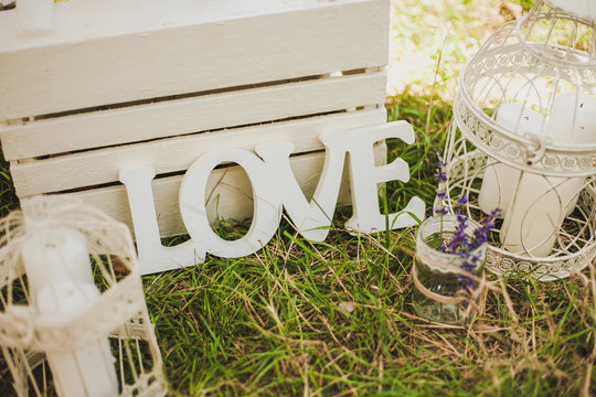 Love - wooden inscription for wedding. Different elements of wedding decor for photo-booth: lanterns, bird cages, candles, flowers on green grass. Color horizontal image.