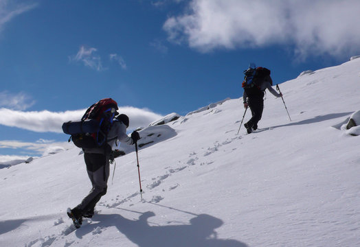 two mountain climbers hiking up a snow slope in the Swiss Alps with a lot of equipment and large backpacks