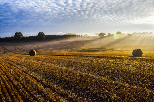 Sonnenaufgang &uuml;ber Norddeutschen Feld. Strohballen mit Sonnenstrahlen. 