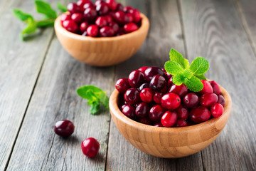 Fresh juicy cranberries in a bamboo bowl on the old wooden background. Selective focus.