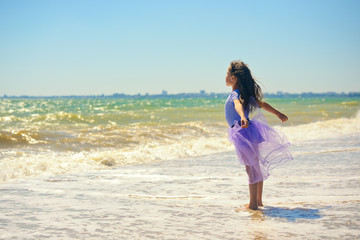 Happy little girl standing on the seashore with outstretched arms and upturned face to the sun. Landscape orientation