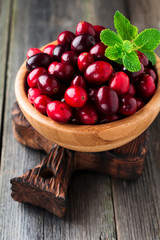 Fresh juicy cranberries in a bamboo bowl on the old wooden background. Selective focus.
