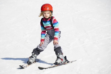 Fototapeta na wymiar Happy child girl enjoying vacation in winter resort. Little girl skiing in mountains. Active sportive toddler wearing helmet learning to ski. Winter sport for family. Skier racing in snow.