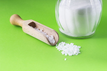 salt crystals with wooden spoon and glass salt shaker on green background