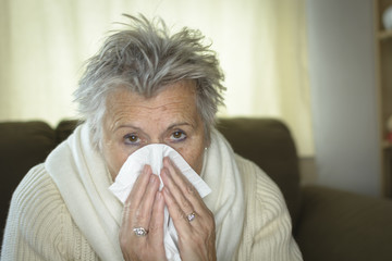 health care, flu, hygiene, age and people concept - sick senior woman blowing nose to paper napkin at home