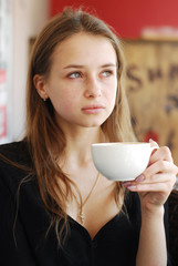 beautiful young girl with a cup of coffee in a coffee shop looki