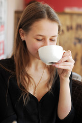 a beautiful young girl drinking coffee in a coffee house