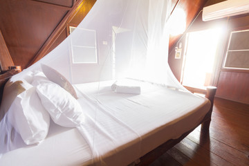 white bed sheets and pillows in net. light passing through a door