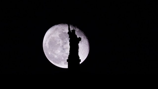 Silhouette of statue of liberty with moon behind