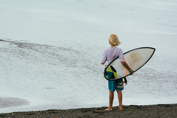 Young surfer holding his surfboard. On his back.