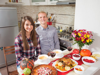 Happy young couple is having a Thanksgiving dinner at home. They are carving roasted turkey and drinking wine.