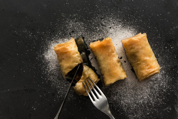 Three baklavas on stone black plate with suggar around, served