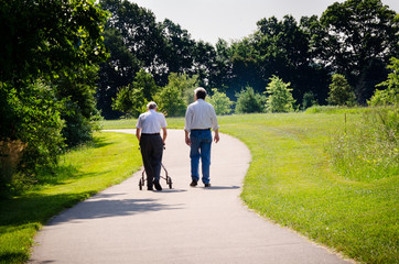 Elderly man using a walker walks a path with a middle aged man.