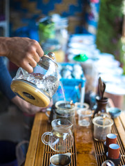 Hand that pours chinese green tea from glass kettle to smal cup, select focus