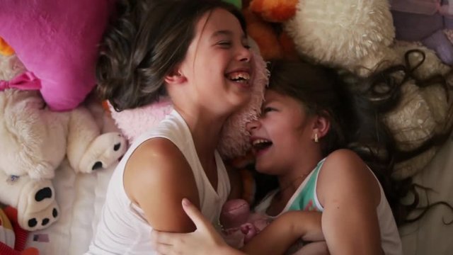 Two little angles are tickling each other in the bed completely covered with soft toys. Two little girls are tickling each other in the bed completely covered with soft toys. Childhood happiness.