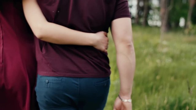 Close-up of womans and mans arms round each other in an embrace. Couple walking in nature. Slow mo, steadicam shot