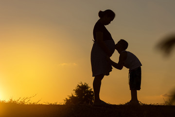 silhouate of happy pragnancy mother with his son playing in suns