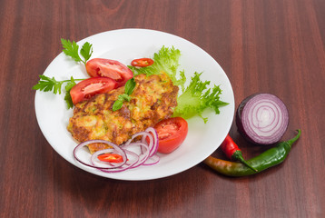 Chopped cutlets and vegetables on white dish on wooden surface