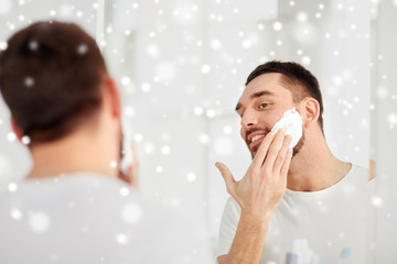 happy man applying shaving foam at bathroom mirror