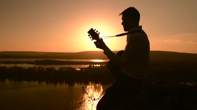Young caucasian muician playing guitar outdoors at sunset time