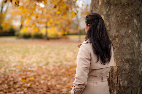 Back of the head image of a mature woman wearing a trench coat in the park watching the fall foliage in autumn with copy space