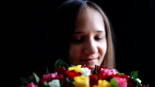 Beautiful smiling woman with a large bouquet of flowers in her arms smelling a fragrant colorful roses on black background. 1920x1080